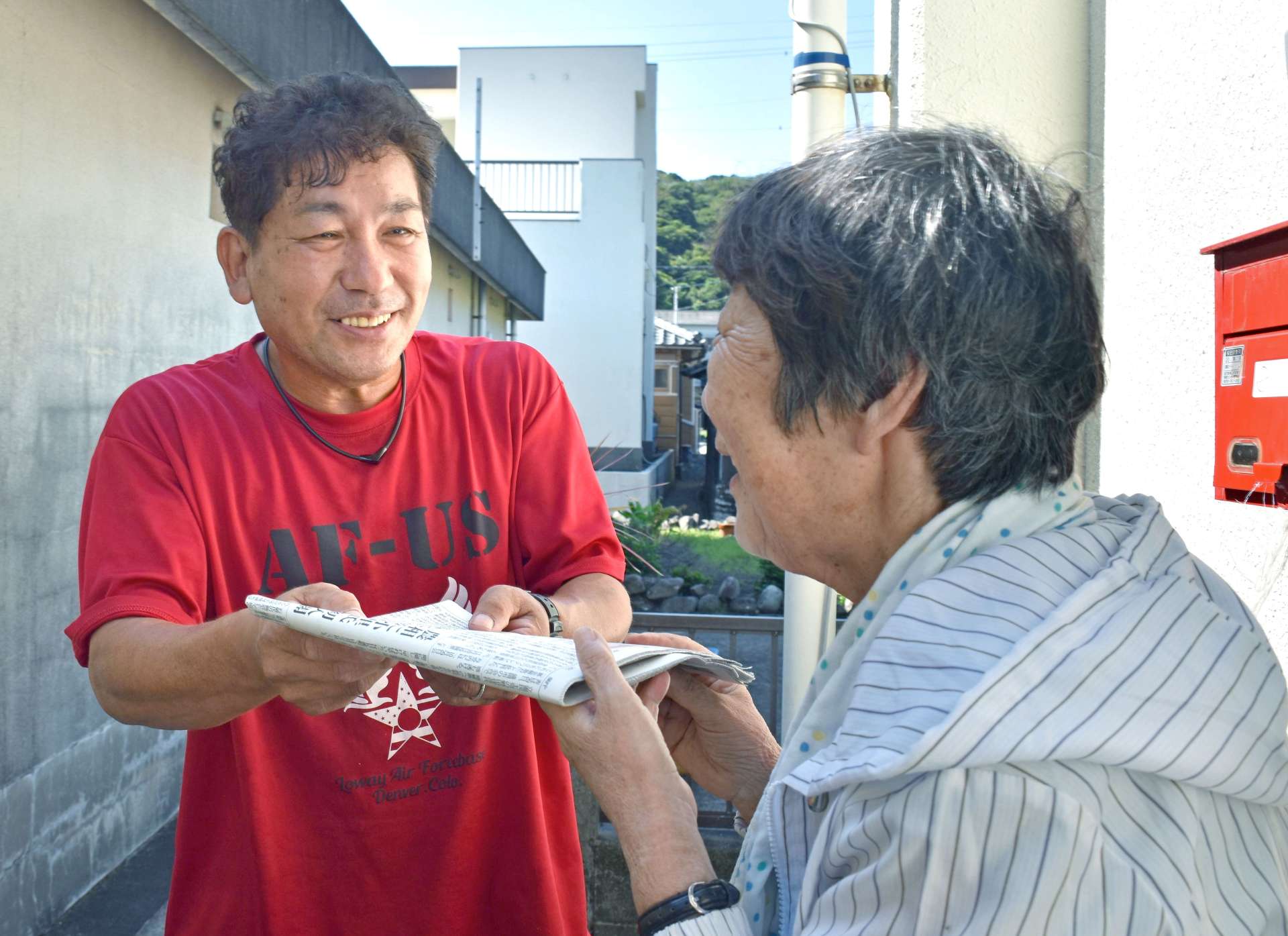 笑顔で新聞を配る川畑兼吾さん（左）＝薩摩川内市上甑町平良