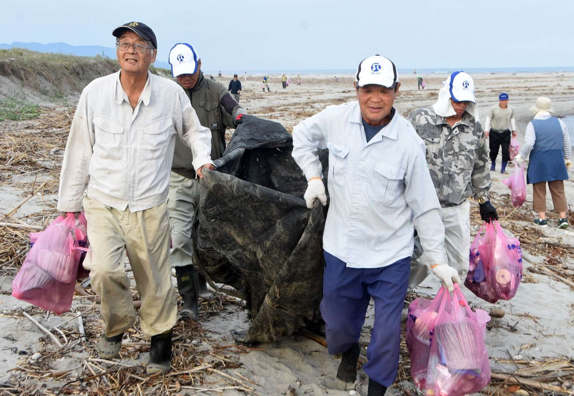 プラスチックごみなどを集めて運ぶシルバー人材センター会員＝南さつま市の新川海岸