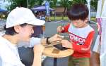 アクセサリー作りの手ほどきを受ける子ども＝阿久根市の風テラスあくね駐車場