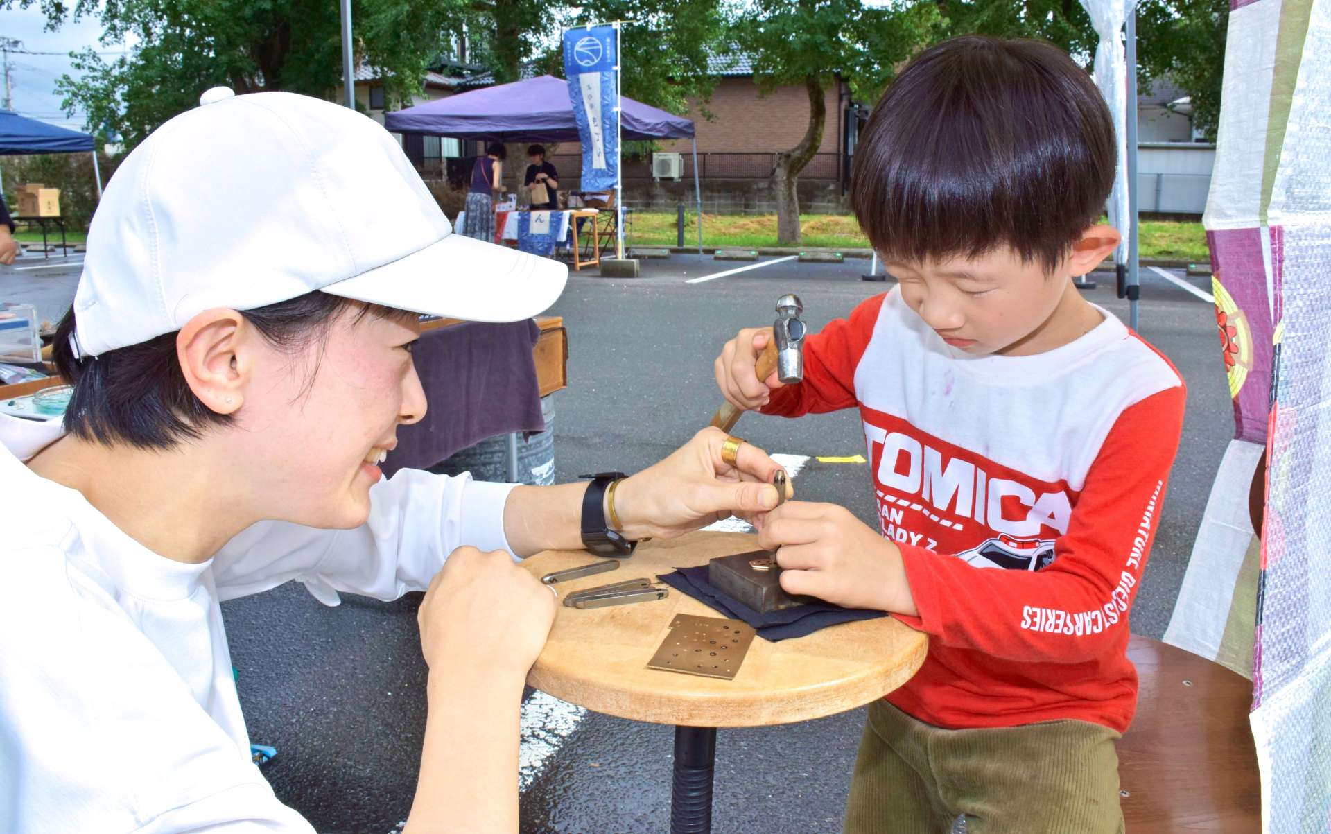 アクセサリー作りの手ほどきを受ける子ども＝阿久根市の風テラスあくね駐車場
