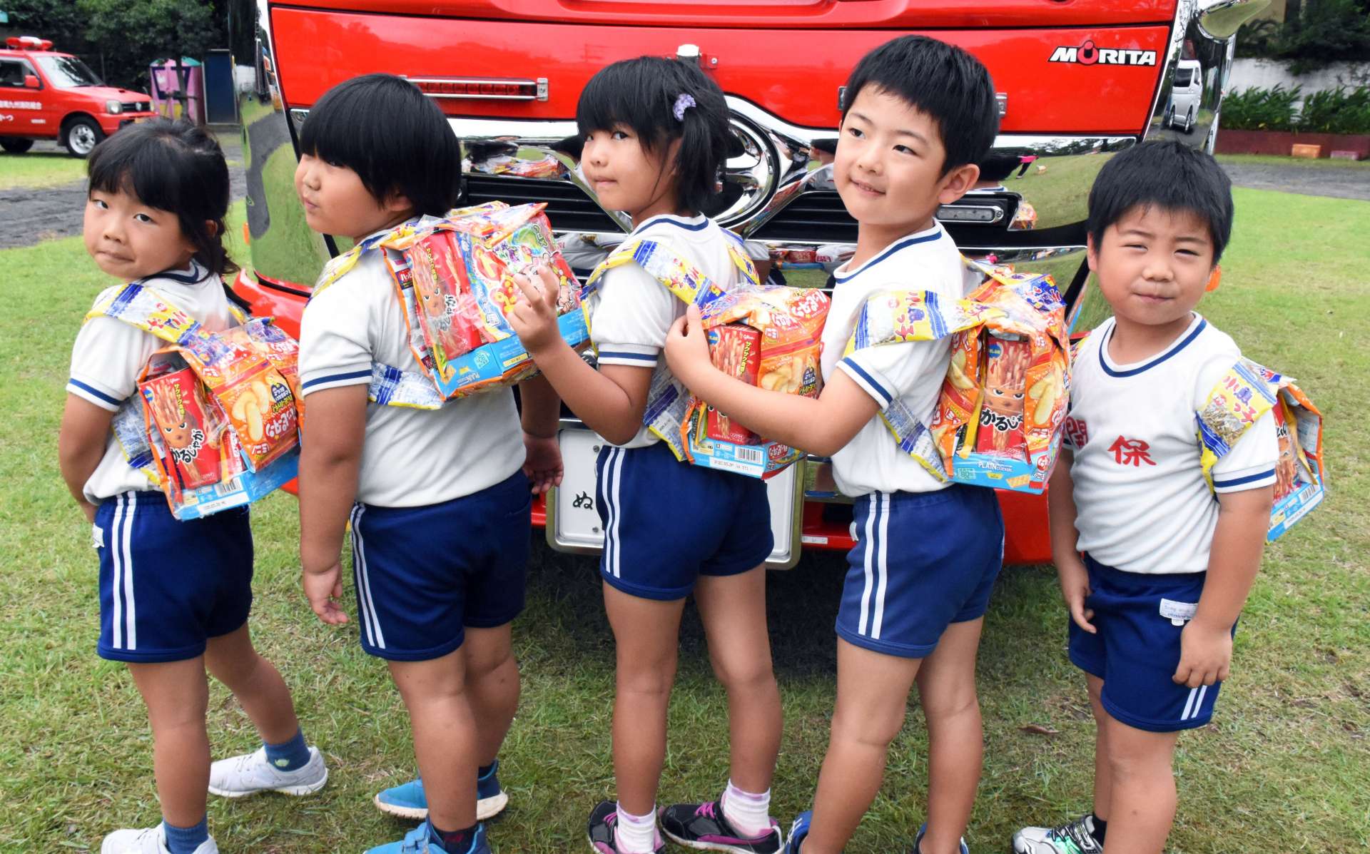 お菓子の防災リュックサックを背負い、笑顔を見せる園児たち＝指宿市の開聞保育園