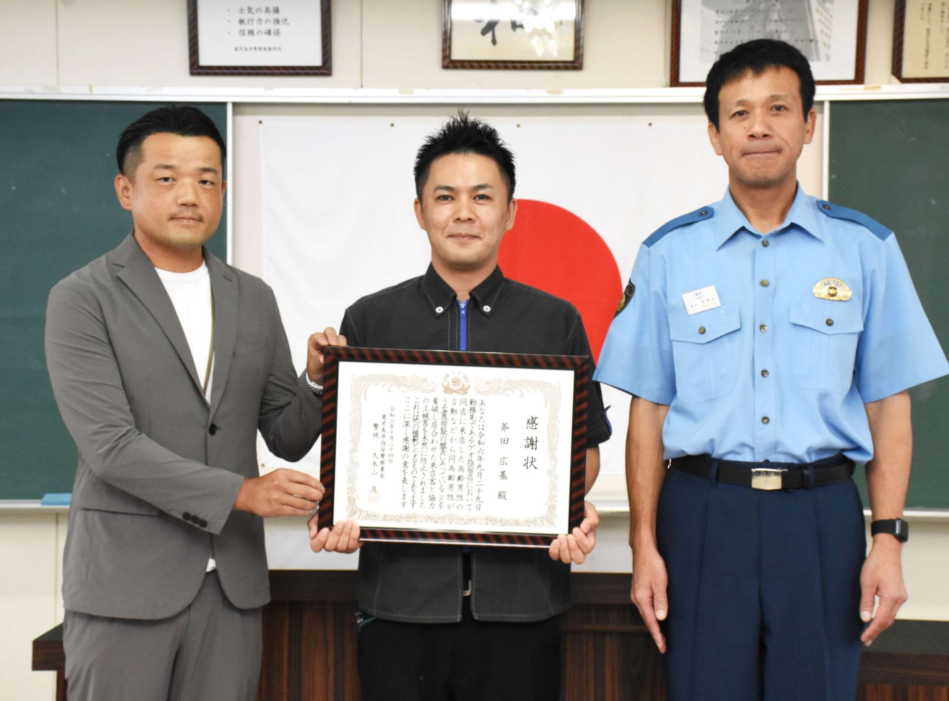 うそ電話詐欺被害を食い止めたゲオ指宿店の斧田広基店長（中央）＝指宿市の指宿警察署