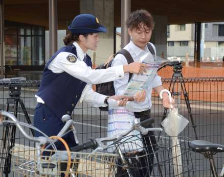 自転車利用者に道交法改正を周知する警察官＝１日、鹿児島市のＪＲ谷山駅
