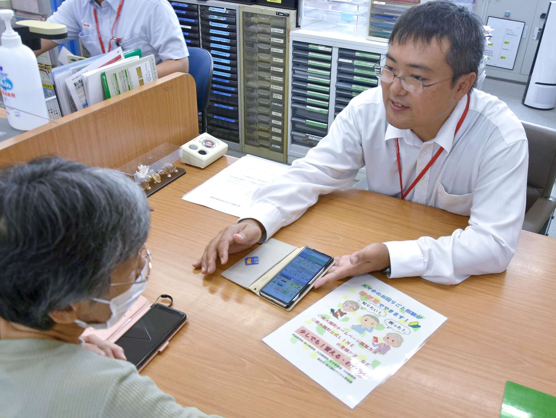 スマートフォンの使い方を説明する大浜郵便局の棈木博之局長（右）＝南大隅町根占山本