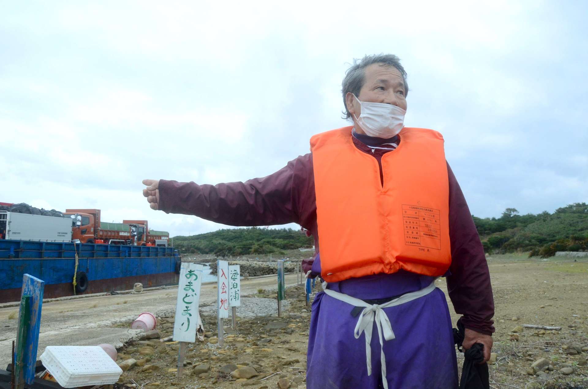 葉山港に停泊する工事関係船舶の前で話をする浜田純男さん＝西之表市馬毛島、１５日午後２時半ごろ