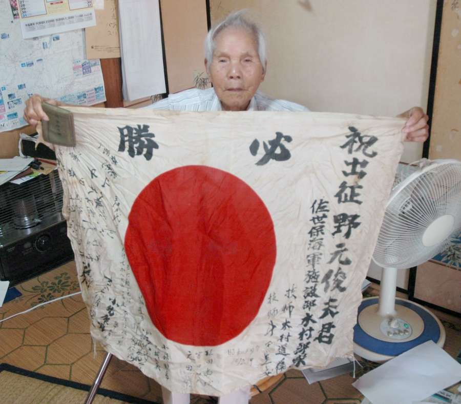 出征時の寄せ書き入り国旗と軍隊手帳を持つ野元俊雄さん＝霧島市牧園
