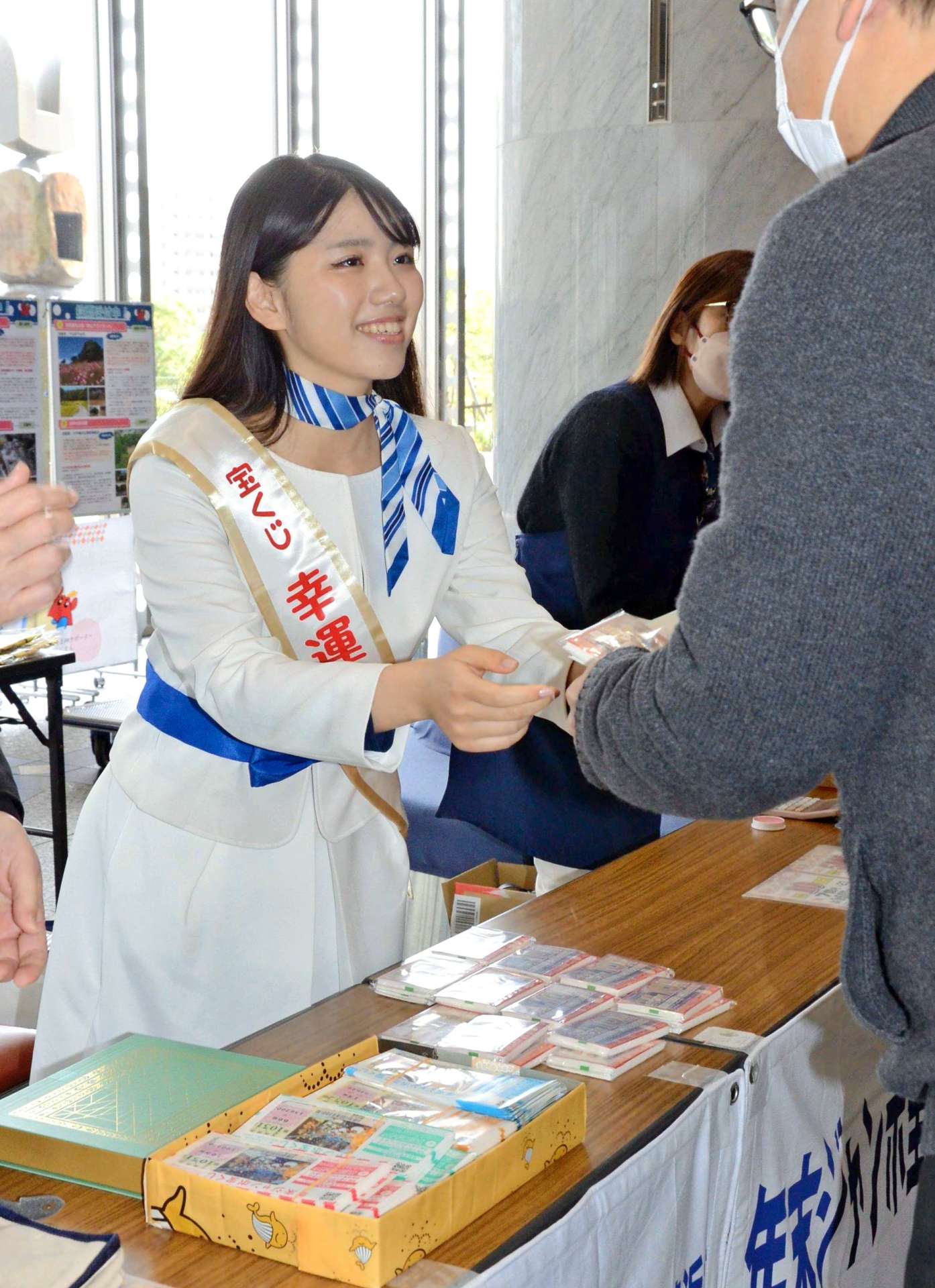 宝くじを手渡す「幸運の女神」の岡田桃果さん＝２８日、県庁