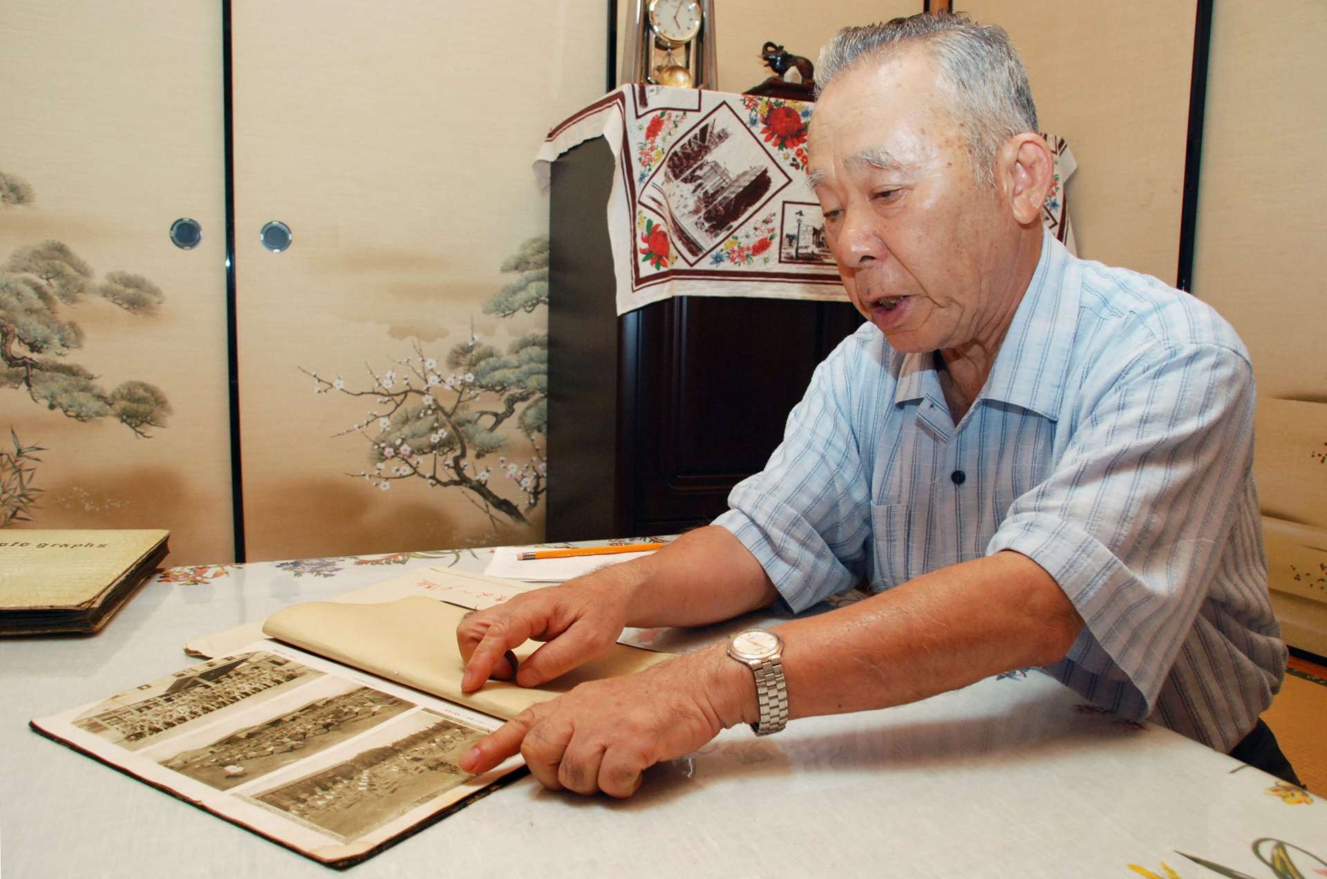 熊本逓信講習所の卒業アルバムを手に経験を語る久留景夫さん＝霧島市国分中央１丁目