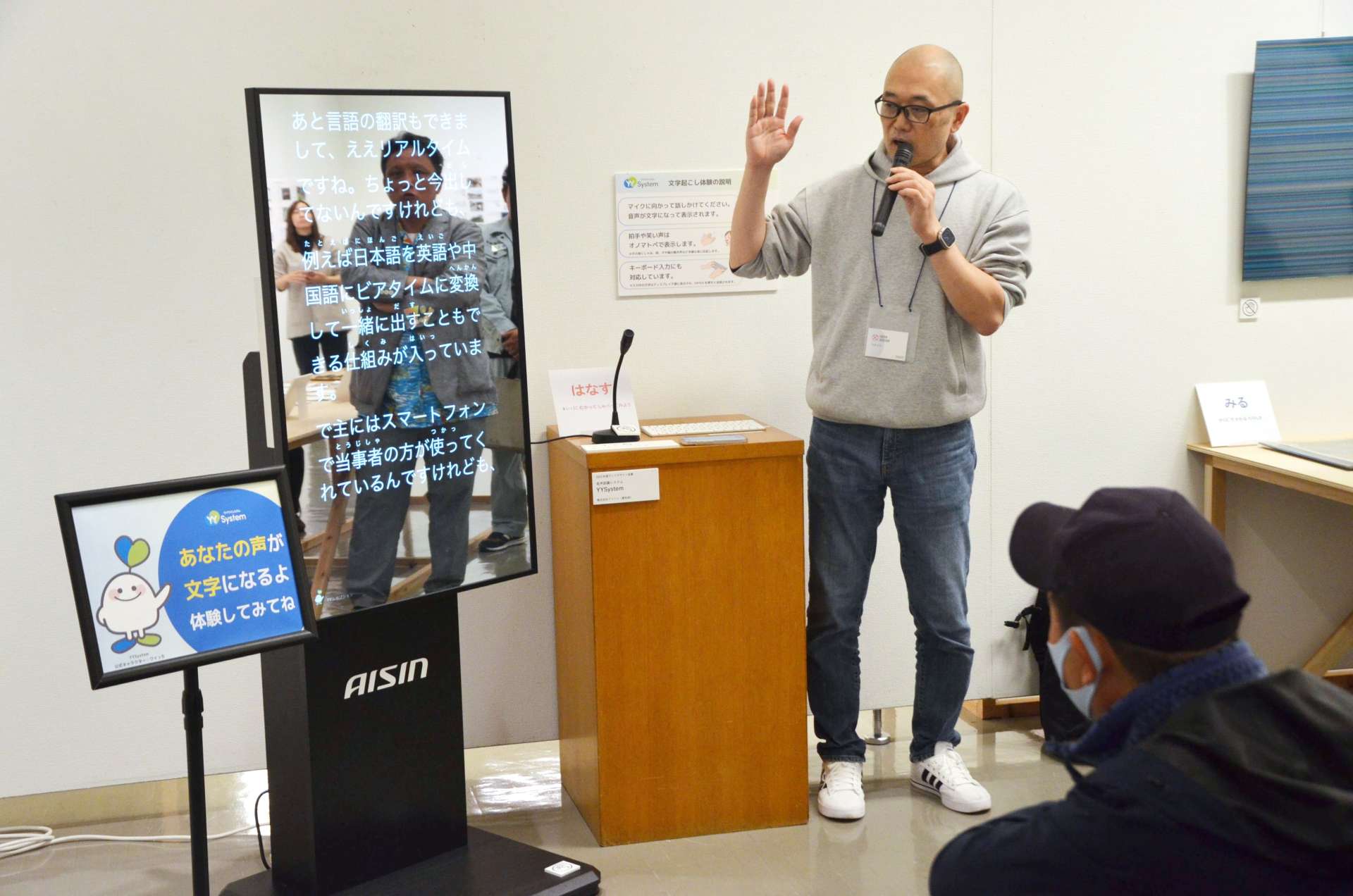 「ＹＹＳｙｓｔｅｍ」開発者の中村正樹さん（写真左）の説明に耳を傾ける来館者＝都城市姫城町の市立美術館
