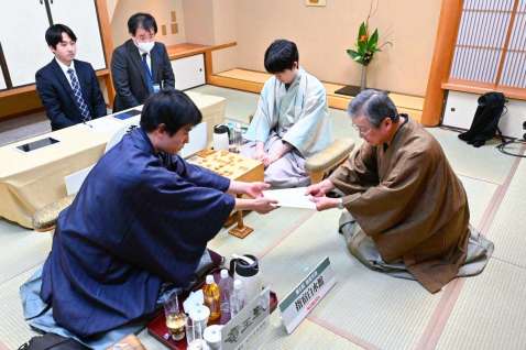 〈関連〉封じ手を立会人に渡す佐々木勇気八段（手前左）＝１１日午後６時すぎ、指宿市の指宿白水館（日本将棋連盟提供）