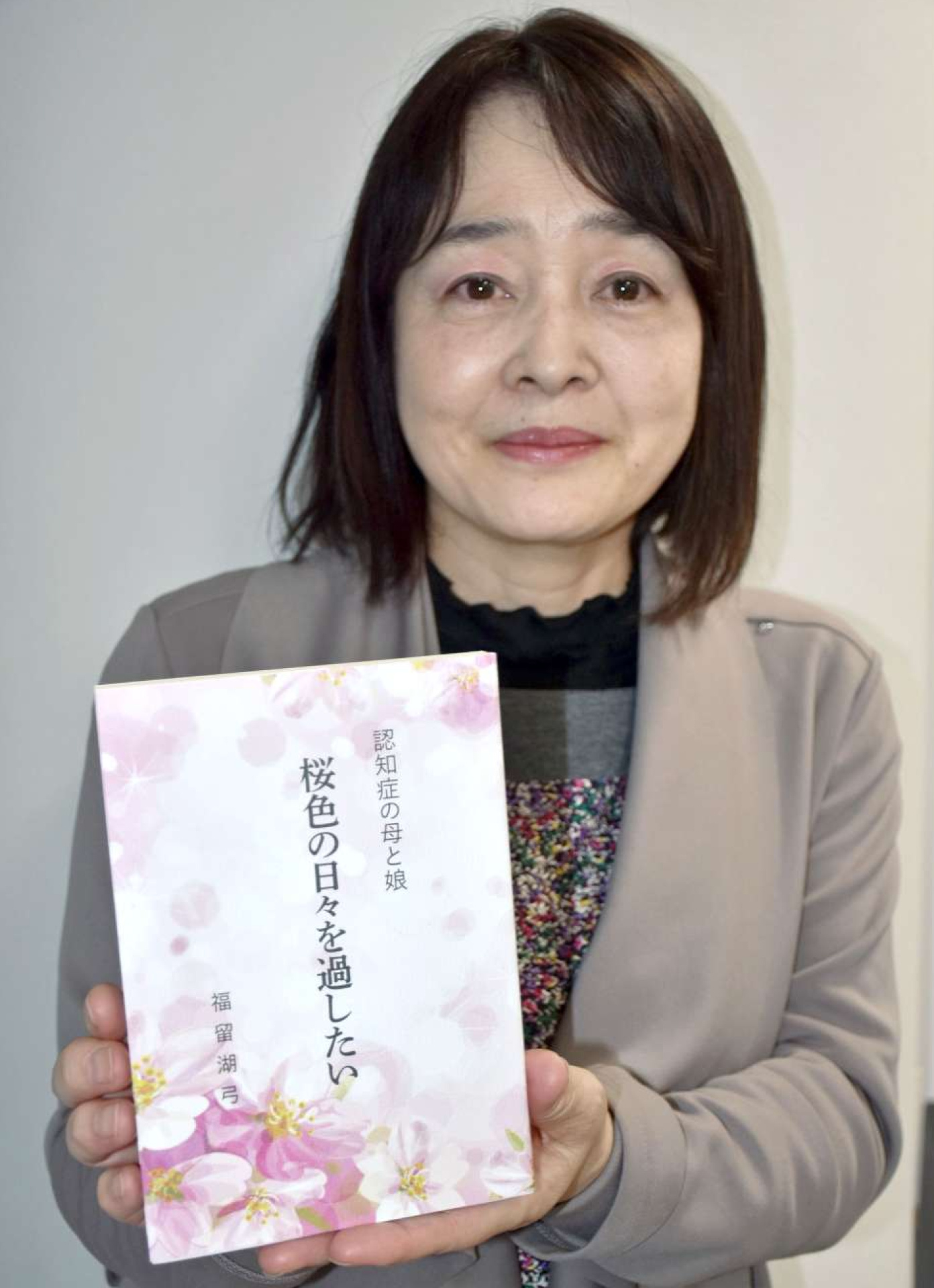 認知症の母の介護体験をまとめた著書を手にする福留湖弓さん＝霧島市