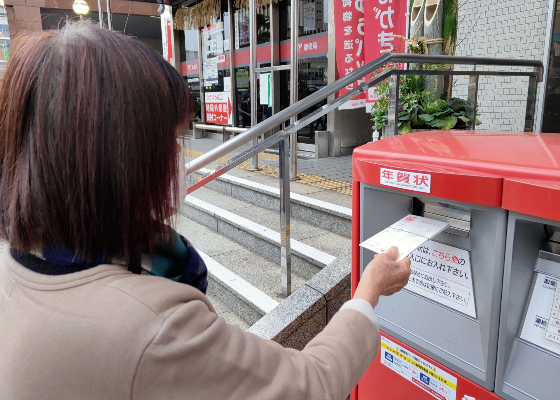 年賀状を郵便ポストに投函する女性＝１５日、鹿児島市の鹿児島中央郵便局（画像の一部を加工しています）