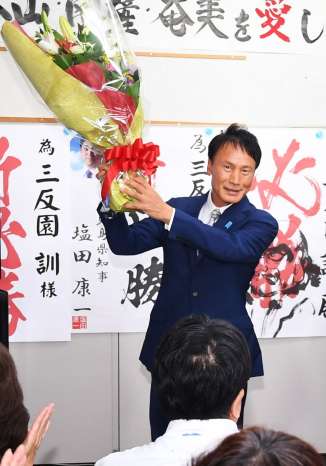 花束を掲げて当選を喜ぶ三反園訓さん＝１０月２７日、鹿児島市谷山中央３丁目