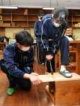 高校生（左）のサポートを受け、板を切る中学生＝出水市の出水中学校