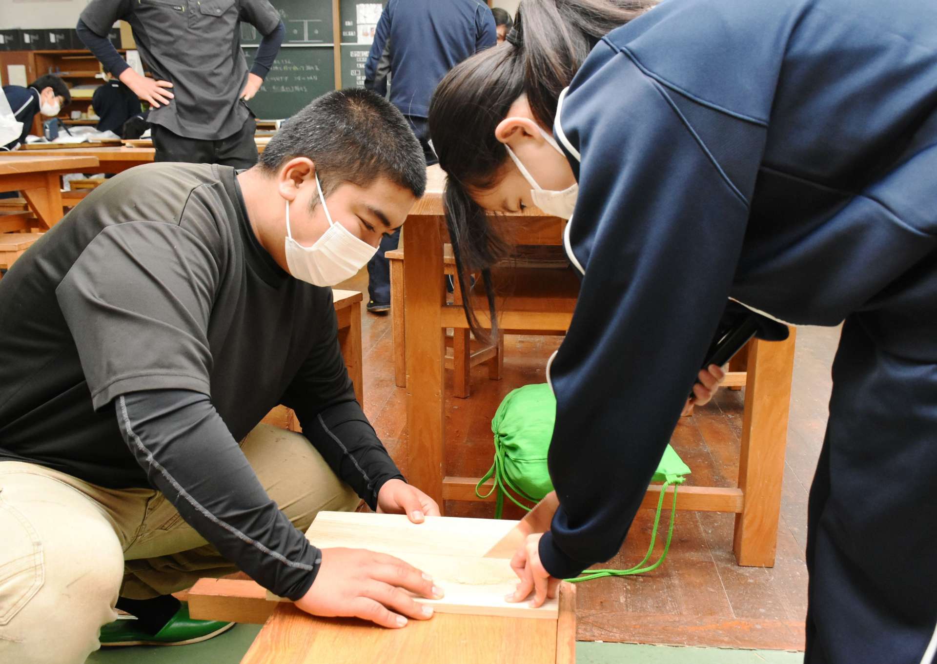 高校生（左）のサポートを受け、板を切る中学生＝出水市の出水中学校