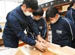 高校生（左）と一緒にかんなで削る中学生＝出水市の出水中学校