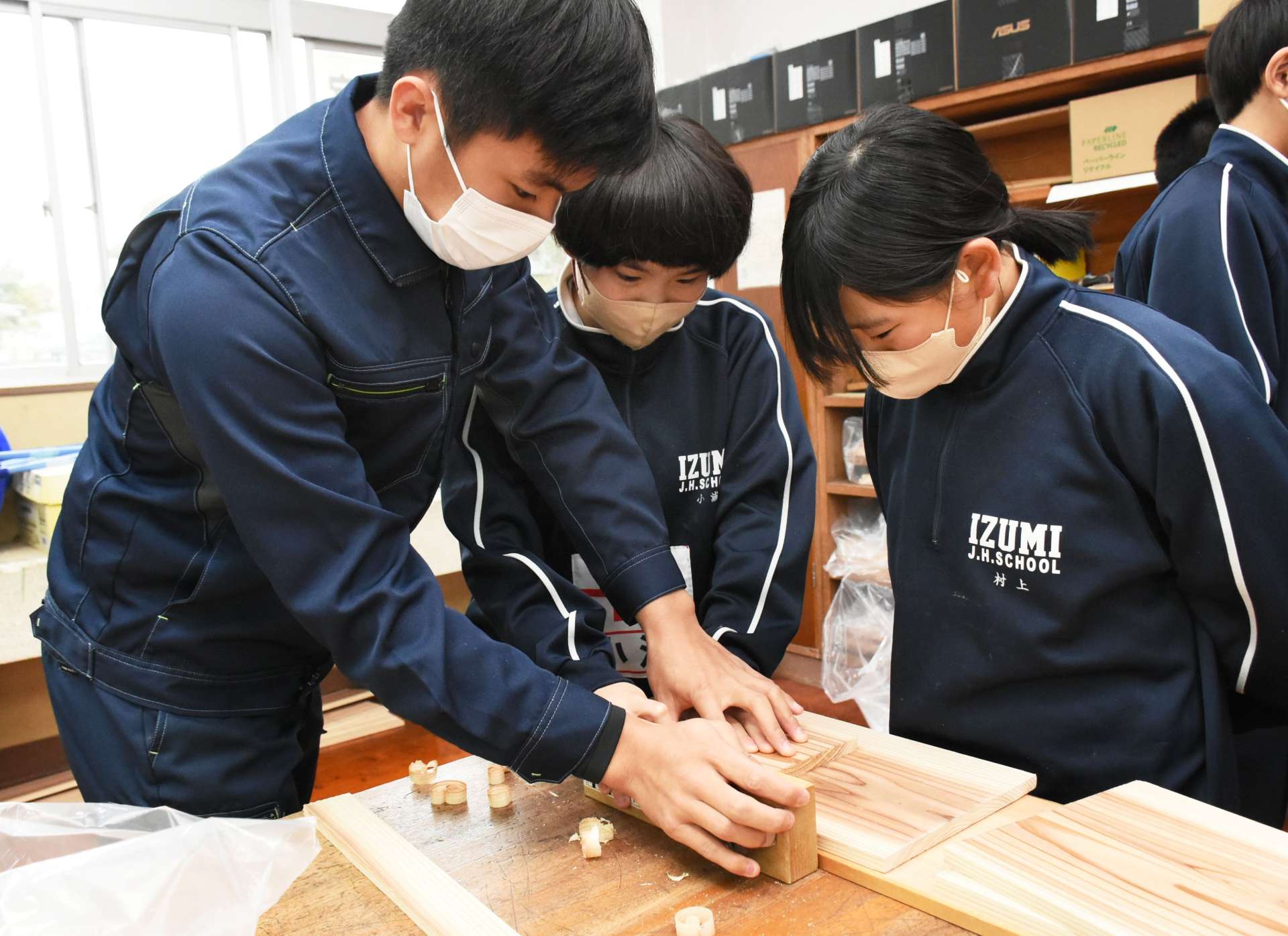 高校生（左）と一緒にかんなで削る中学生＝出水市の出水中学校