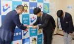 鹿城西高サッカー部の新田祐輔監督（中央）に補助金１００万円の目録を手渡す永山由高・日置市長＝市役所