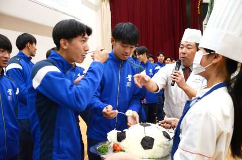 〈別カット〉白星を重ねられるようサプライズで出されたかつお節入りのサッカーボール状にした白米を頬張るサッカー部員ら＝２４日、日置市の鹿児島城西高校
