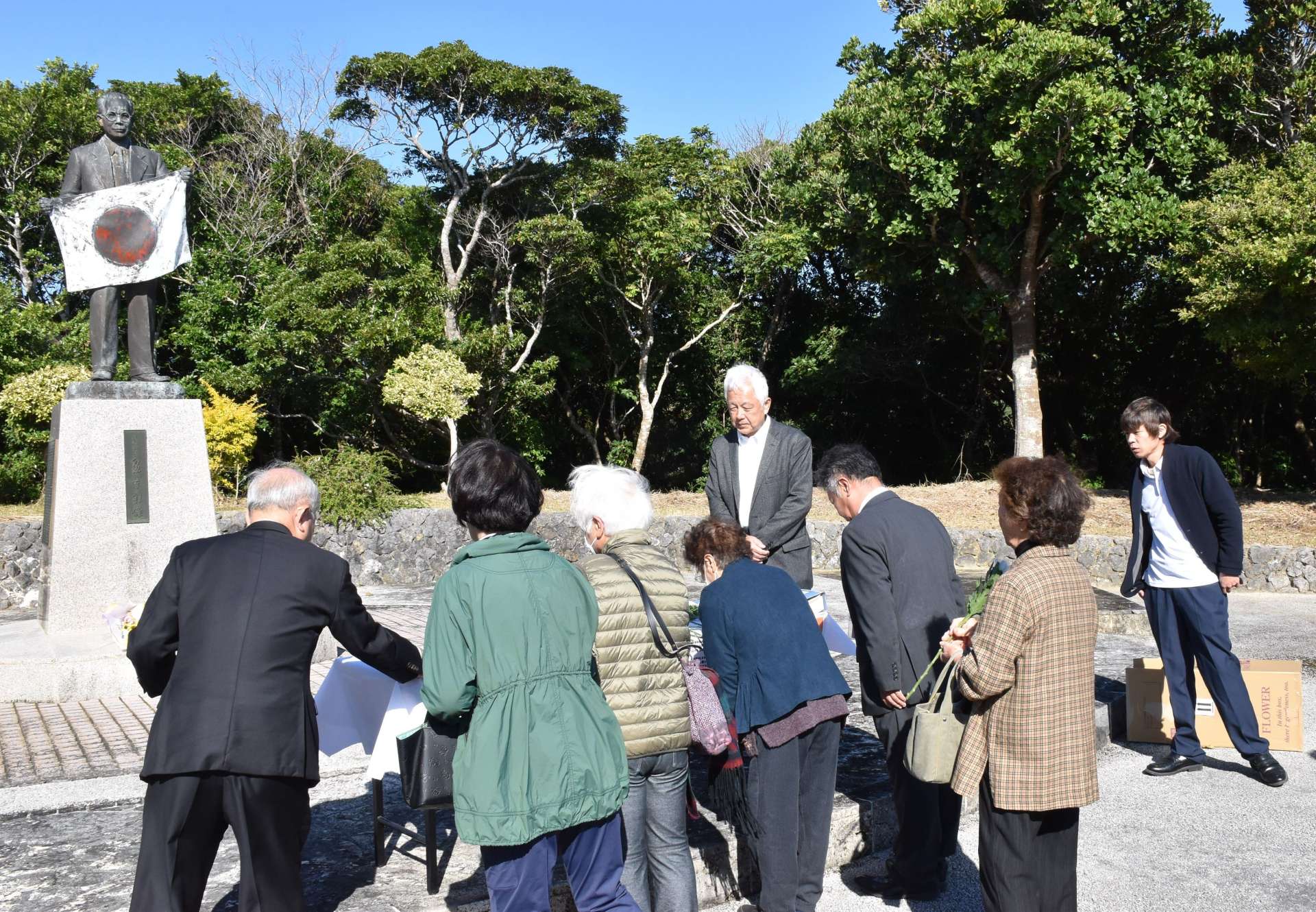 泉芳朗頌徳記念像に献花する参加者＝２５日、伊仙町伊仙の義名山公園