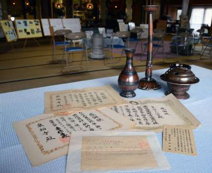 金属供出に対する「陸軍大臣東條英機」の感謝状や梵鐘回収の受領調書、陶器製の代用仏具など、泉福寺に残る戦時中の資料＝さつま町永野の泉福寺