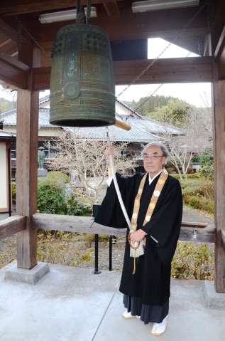 泉福寺の鐘楼につるされた小型の半鐘を、「恒久平和を願ってつく」と語る横井晃仁住職＝さつま町永野