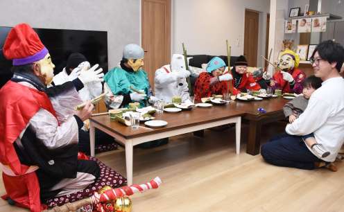 長くて大きな竹箸を持ち、もてなしの膳と格闘する七福神＝１１日夜、霧島市国分福島３丁目