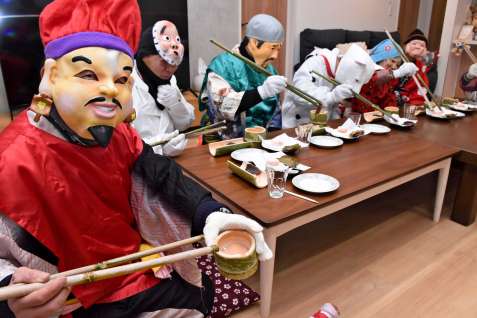 長くて大きな竹箸を持ち、もてなしの膳と格闘する七福神＝１１日夜、霧島市国分福島３丁目