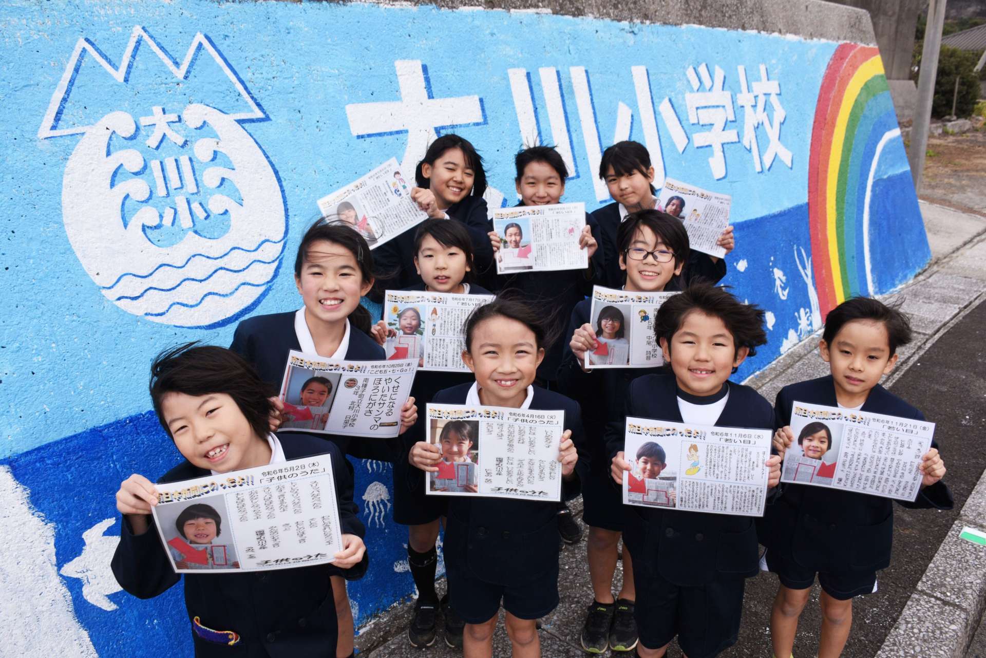 新聞掲載された作品のラミネートを手に笑顔を見せる児童たち＝南種子町の大川小学校