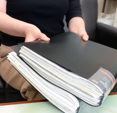 告発のために集めた資料を手にする４０代女性＝２０２４年１０月、志布志市内