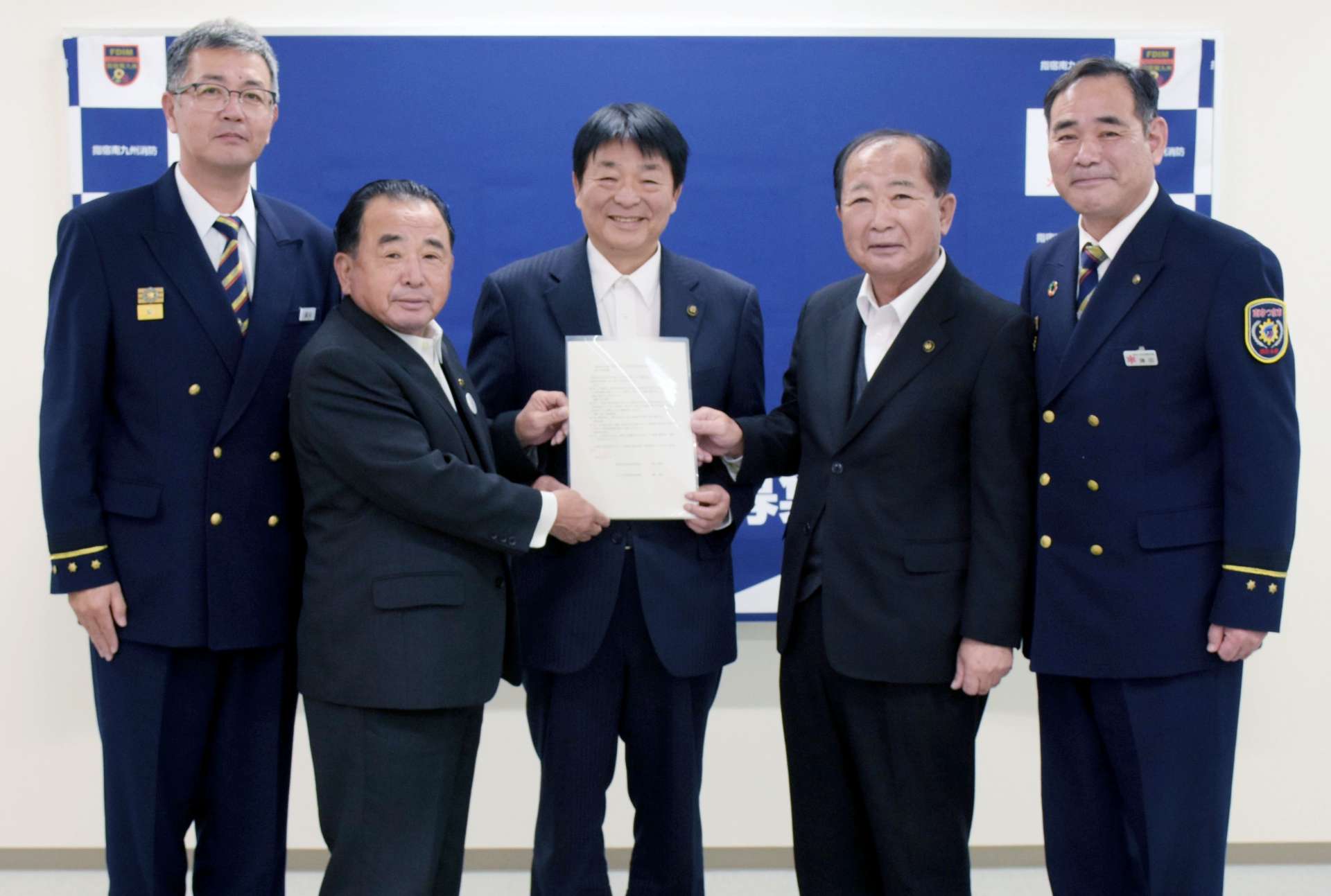 連携強化について定めた協定書を手に笑顔を見せる関係者＝２７日、南九州市の南九州消防署