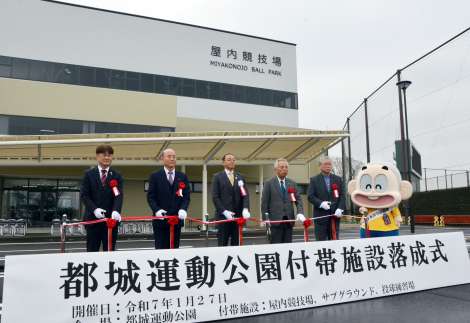 新築された屋内競技場前でテープカットする関係者＝２７日、都城市妻ケ丘町