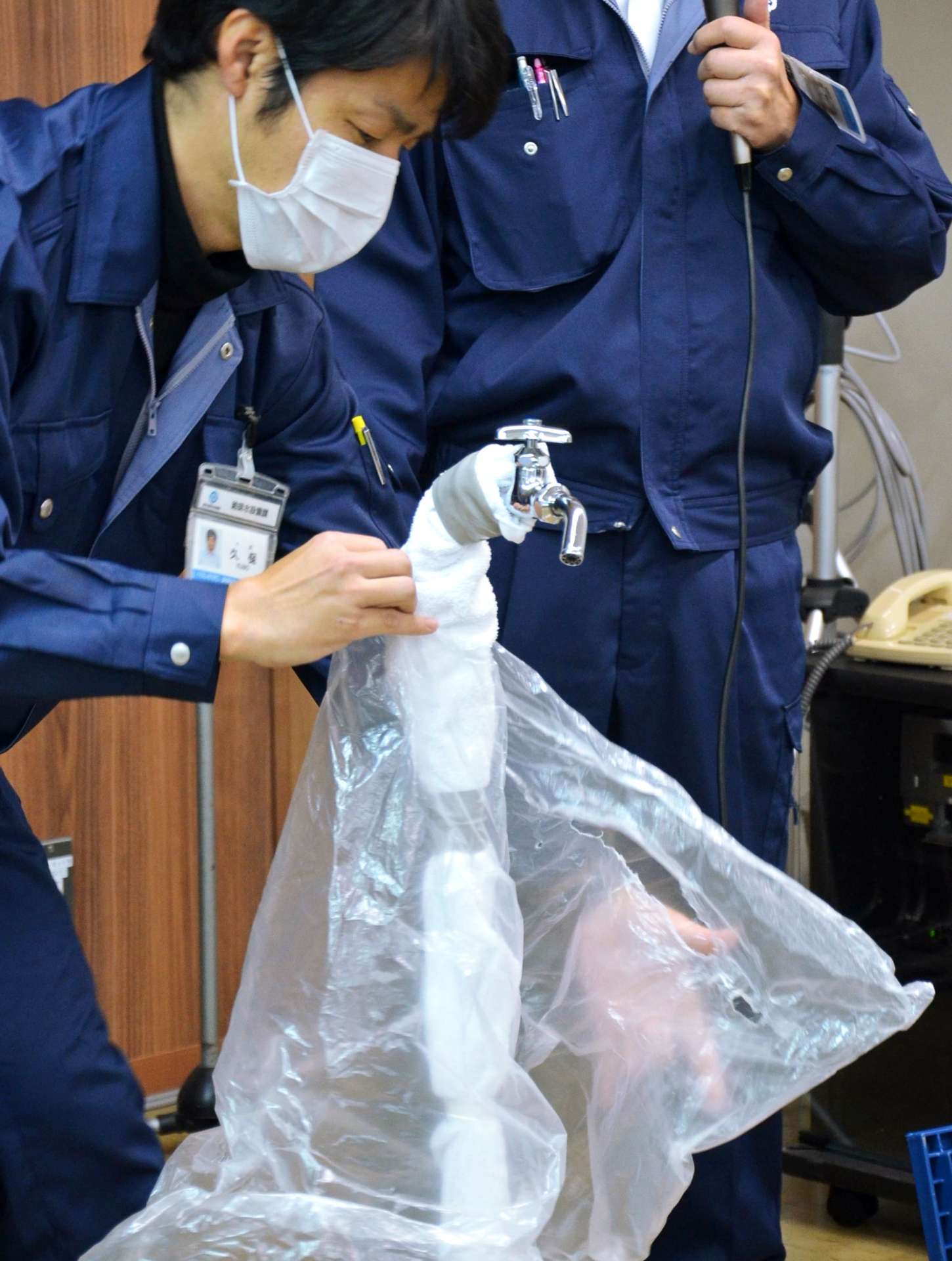 水道管にタオルやビニール袋を巻き、凍結対策を実演する鹿児島市水道局の職員＝３日、同市鴨池新町
