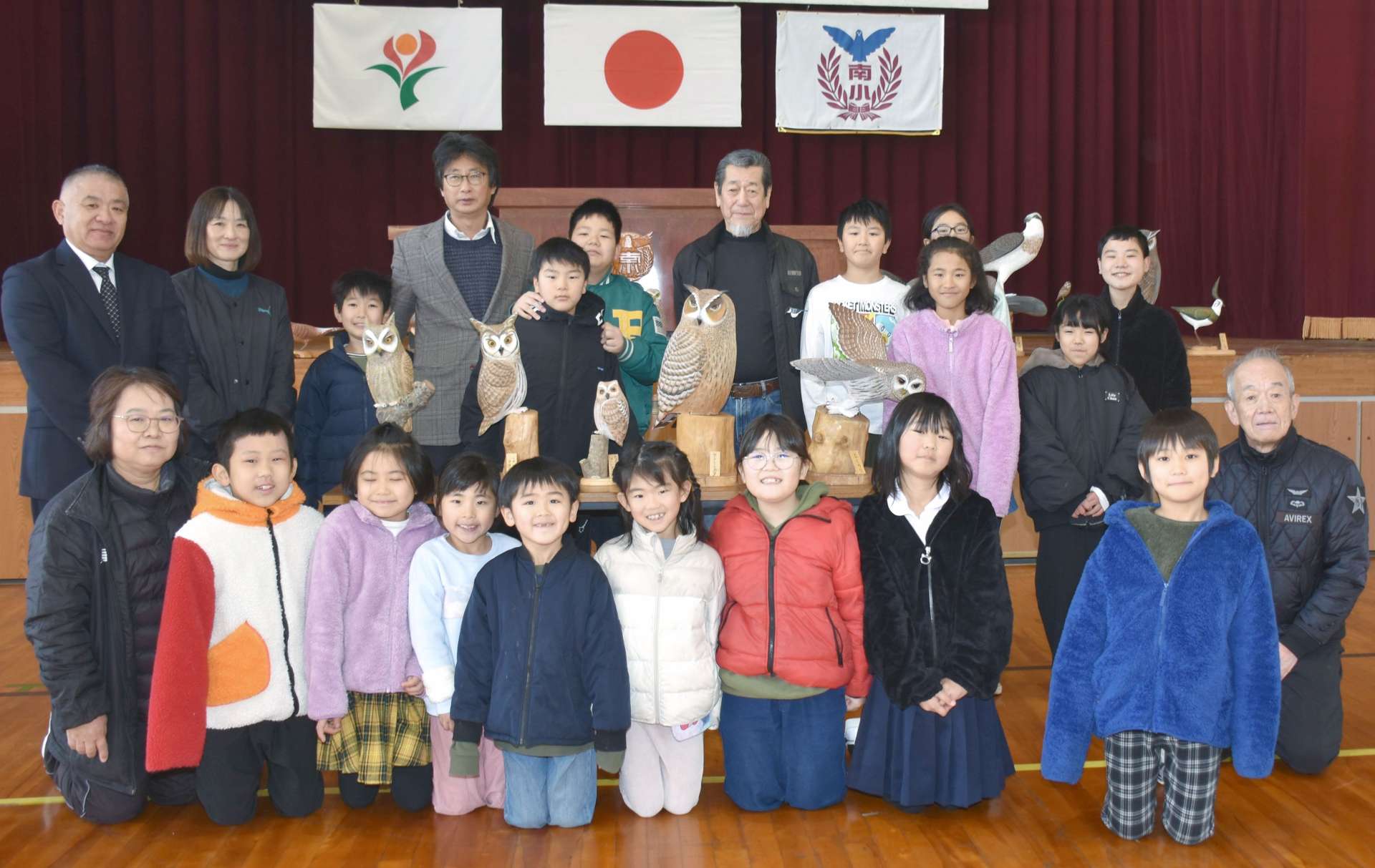 木彫りのフクロウなどを贈った畠野尚利さん（中央）を囲む児童ら