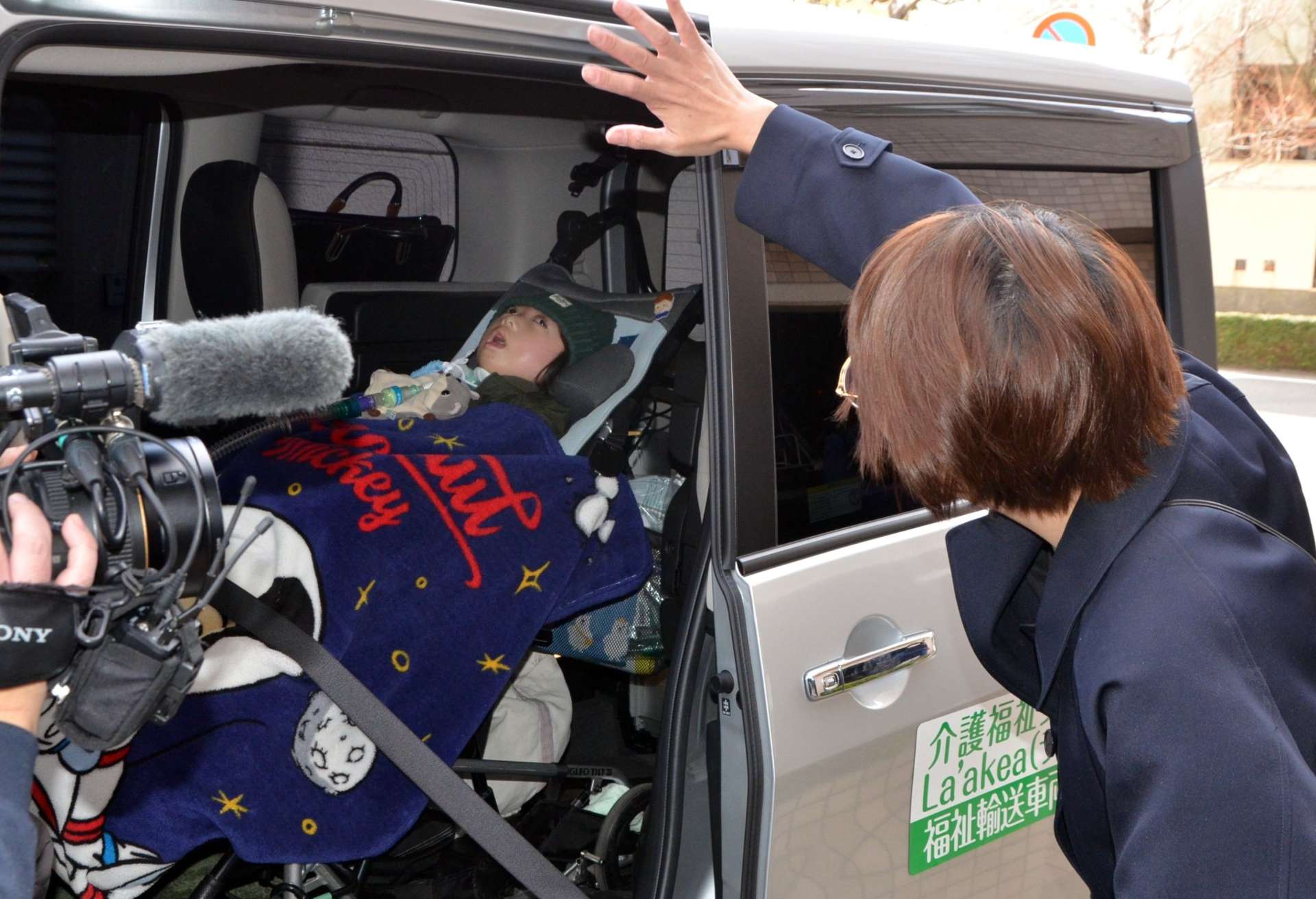 福祉タクシーで学校に向かう柿内瑛斗さんに手を振る母親の祥子さん＝１月２０日、鹿児島市