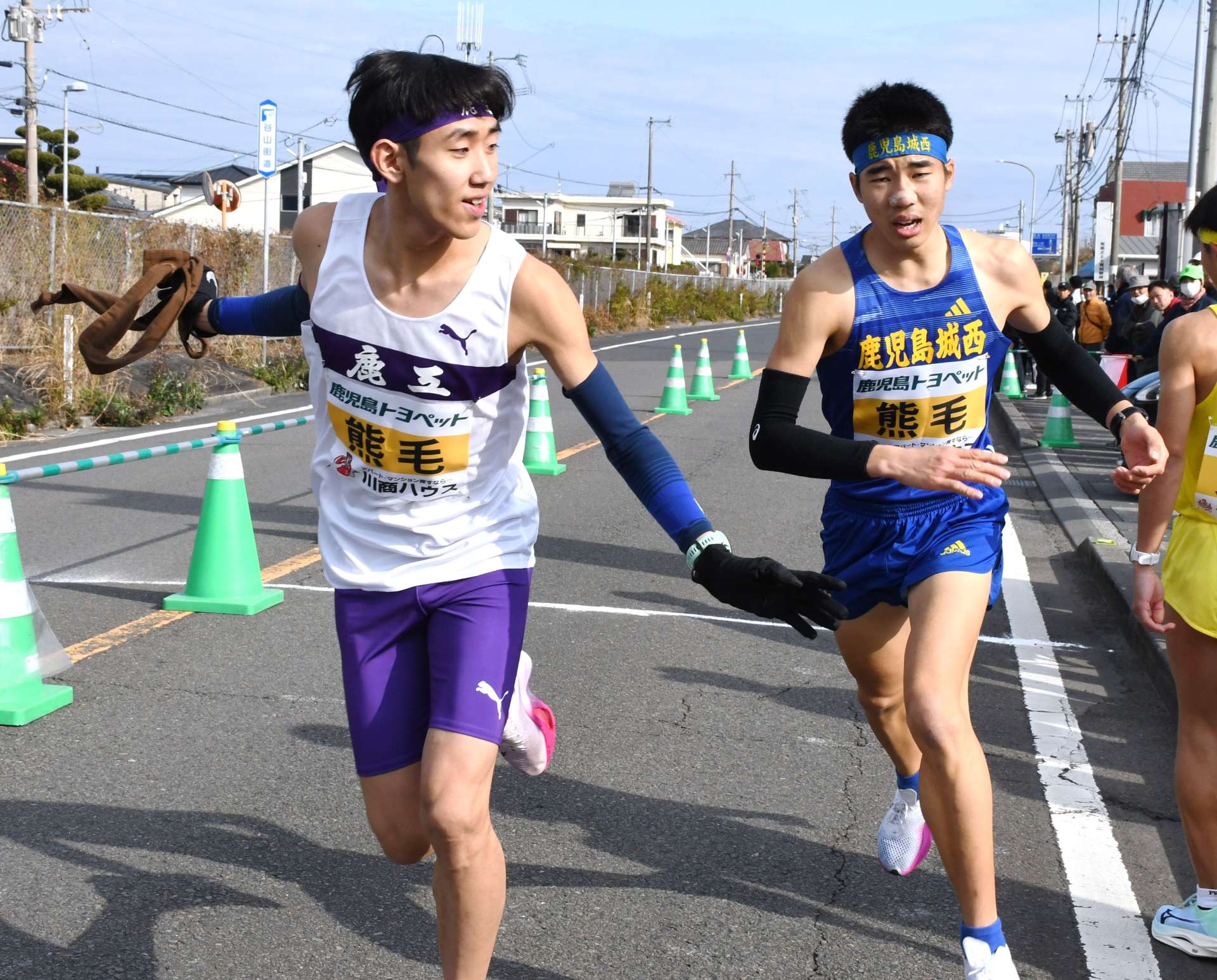 第１中継所、高校３年生同士でたすきをつなぐ熊毛の山口寛太郎選手（右）と牛原幸英選手＝１５日午前、鹿児島市坂之上５丁目
