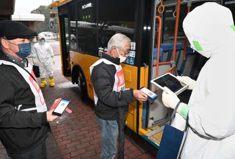 スマートフォン画面のＱＲコードを示し、避難バスに乗り込む訓練参加者＝１６日、鹿児島市郡山町の郡山中央構造改善センター