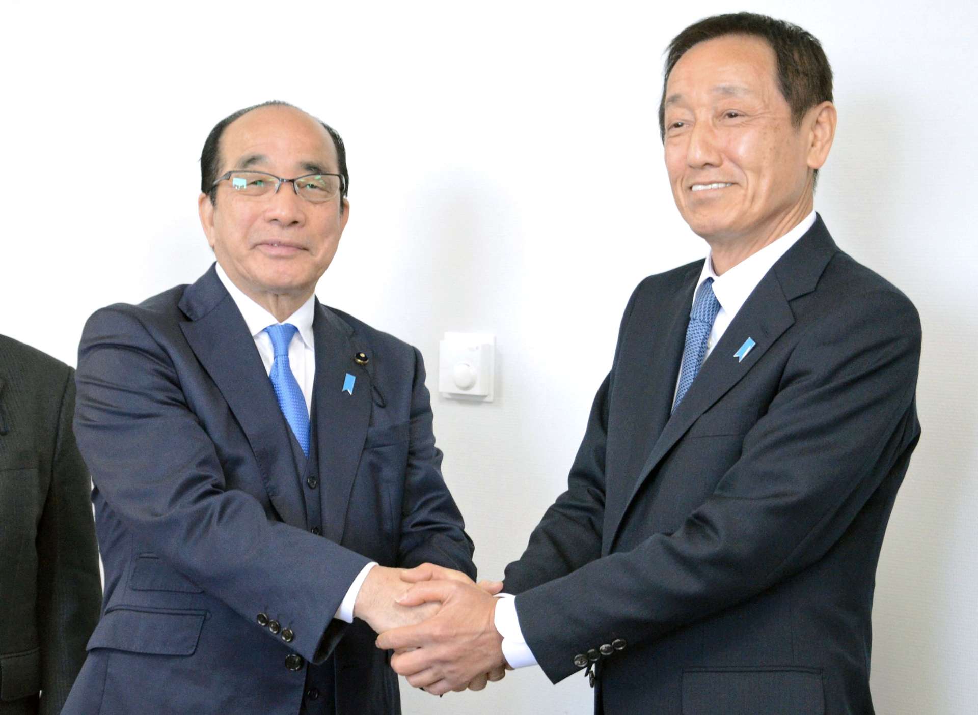 報道陣を前に笑顔で握手を交わす外薗勝蔵氏（左）と園田修光氏＝１９日、県議会