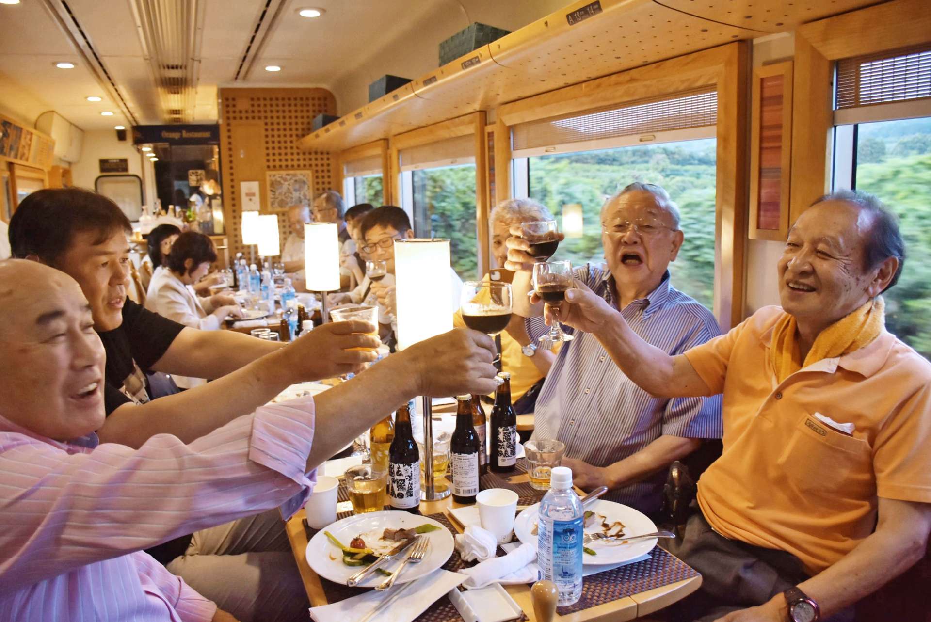 夕焼けの海を眺めながらビールで乾杯する乗客ら＝２０２４年６月、肥薩おれんじ鉄道のおれんじ食堂車内