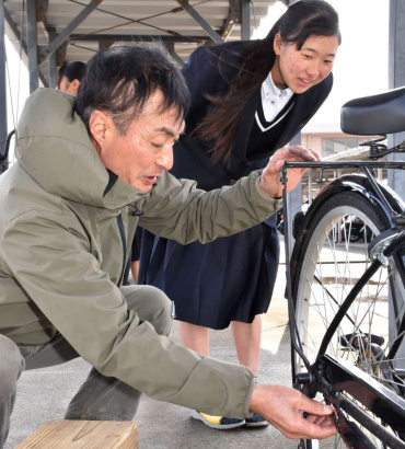 生徒と会話しながら自転車を整備する有岡直生さん＝薩摩川内市の川内高校