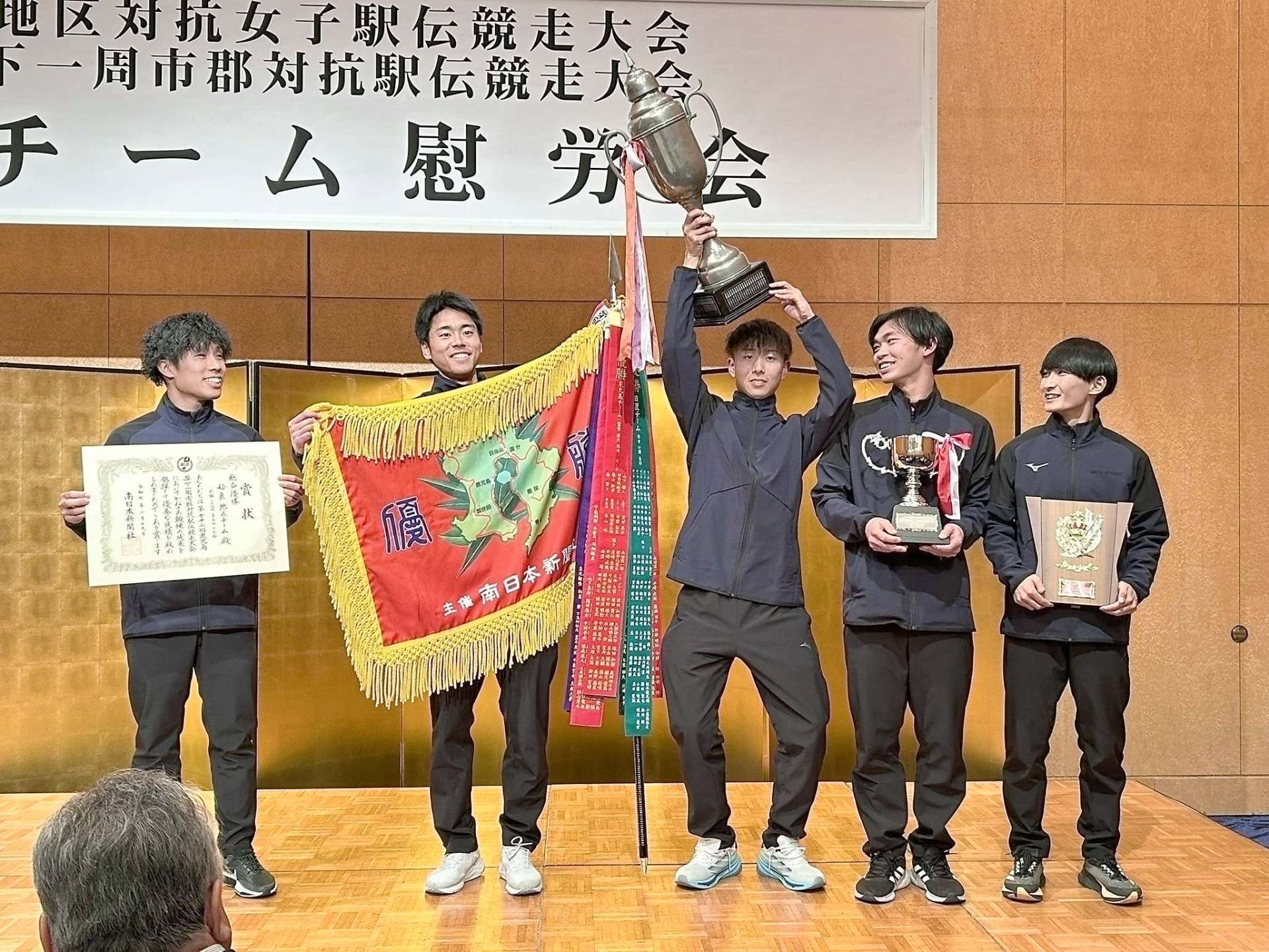 トロフィーや優勝旗を持ち総合優勝を喜ぶ姶良チームメンバー＝１９日、霧島市のホテル京セラ