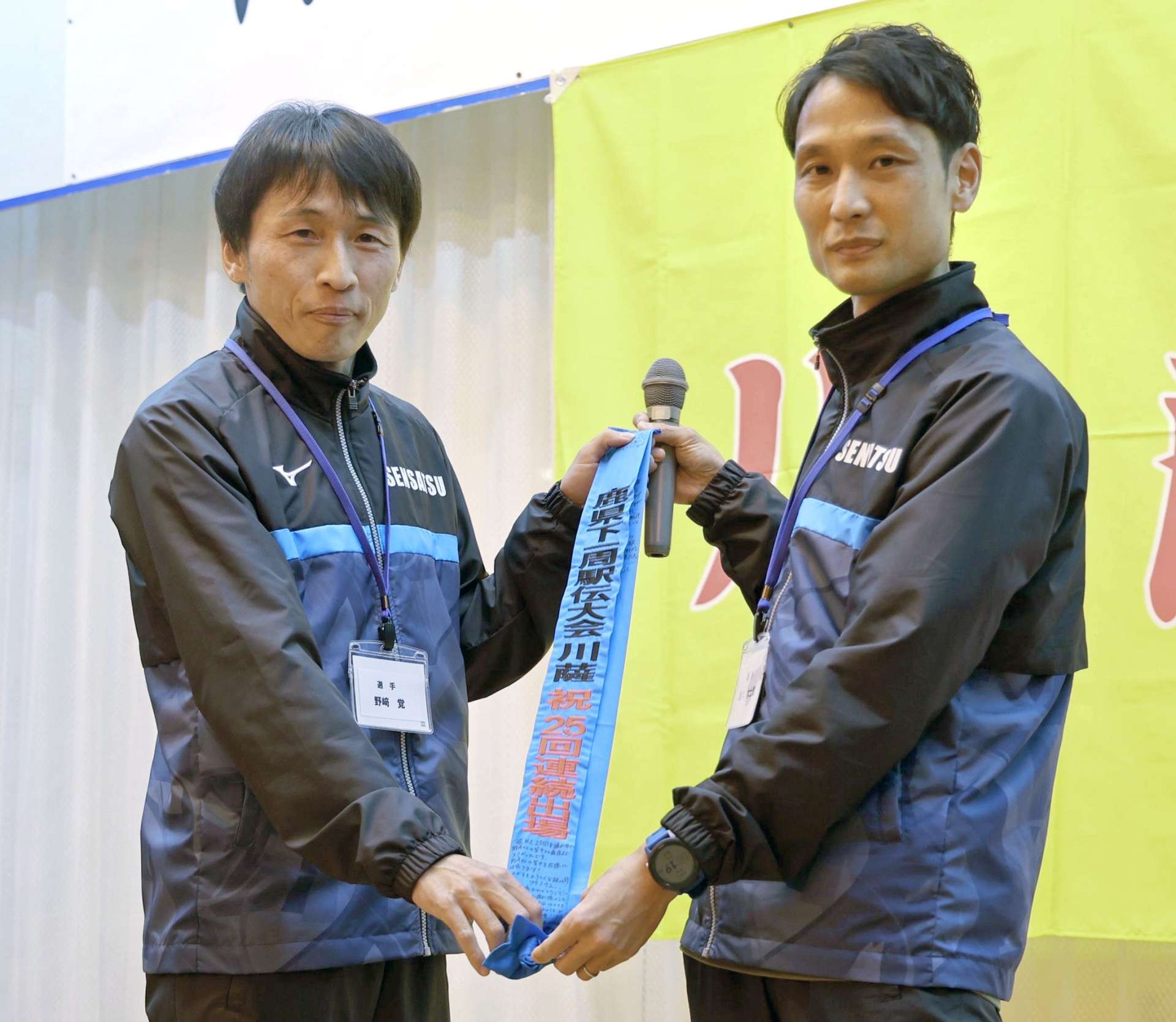 特製のたすきを受け取る野崎（左）＝１９日、薩摩川内市のホテルオートリ