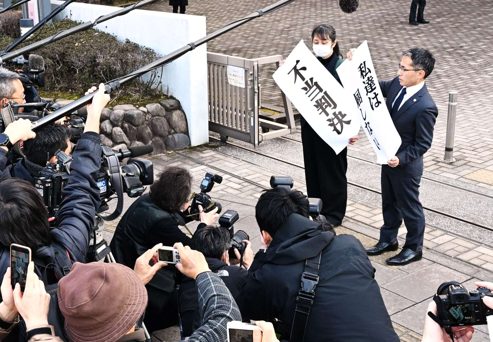 「不当判決」と書かれた紙を掲げる原告団＝２１日午後、鹿児島市の鹿児島地方裁判所