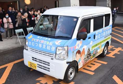 出発式で宅配の専用車を見送る関係者＝１９日、南さつま市加世田