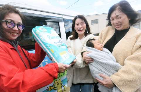 おむつの宅配を生協職員から受け取る家族＝南さつま市加世田