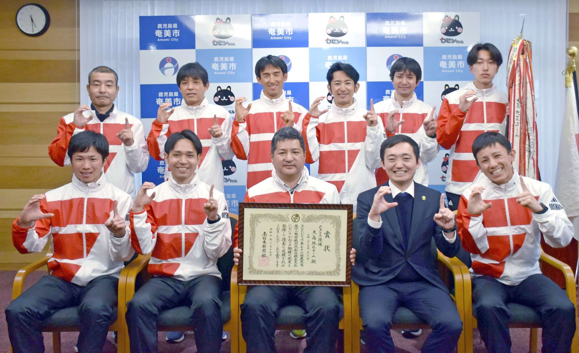 奄美市の安田壮平市長（手前右から２人目）にＣ級優勝を報告する大島チーム＝２５日、同市役所