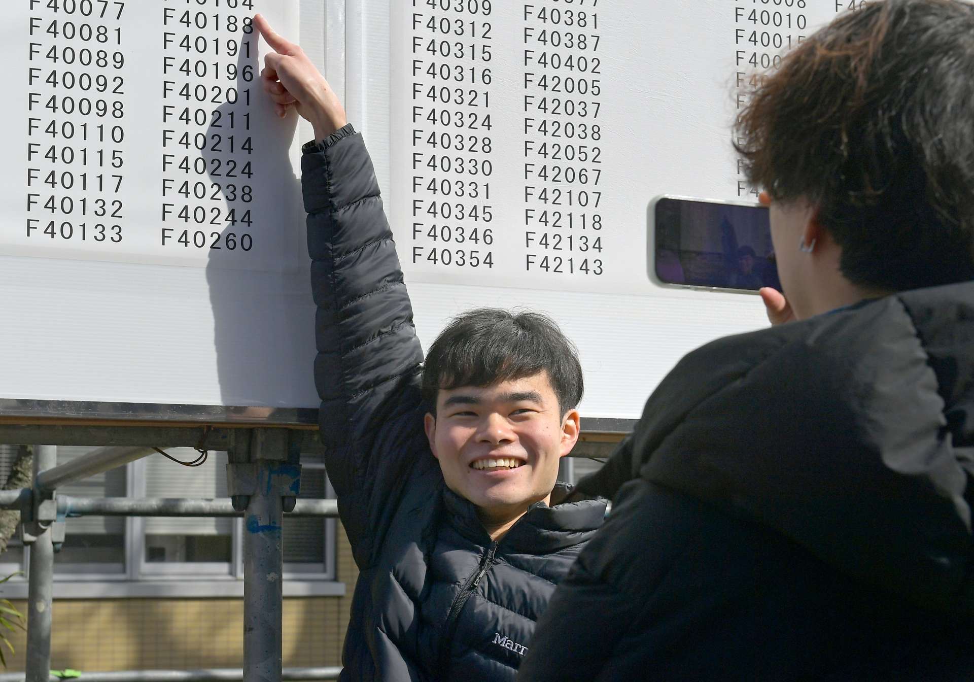 自分の番号を確認し笑顔で記念撮影する受験生＝７日、鹿児島市郡元１丁目の鹿児島大学
