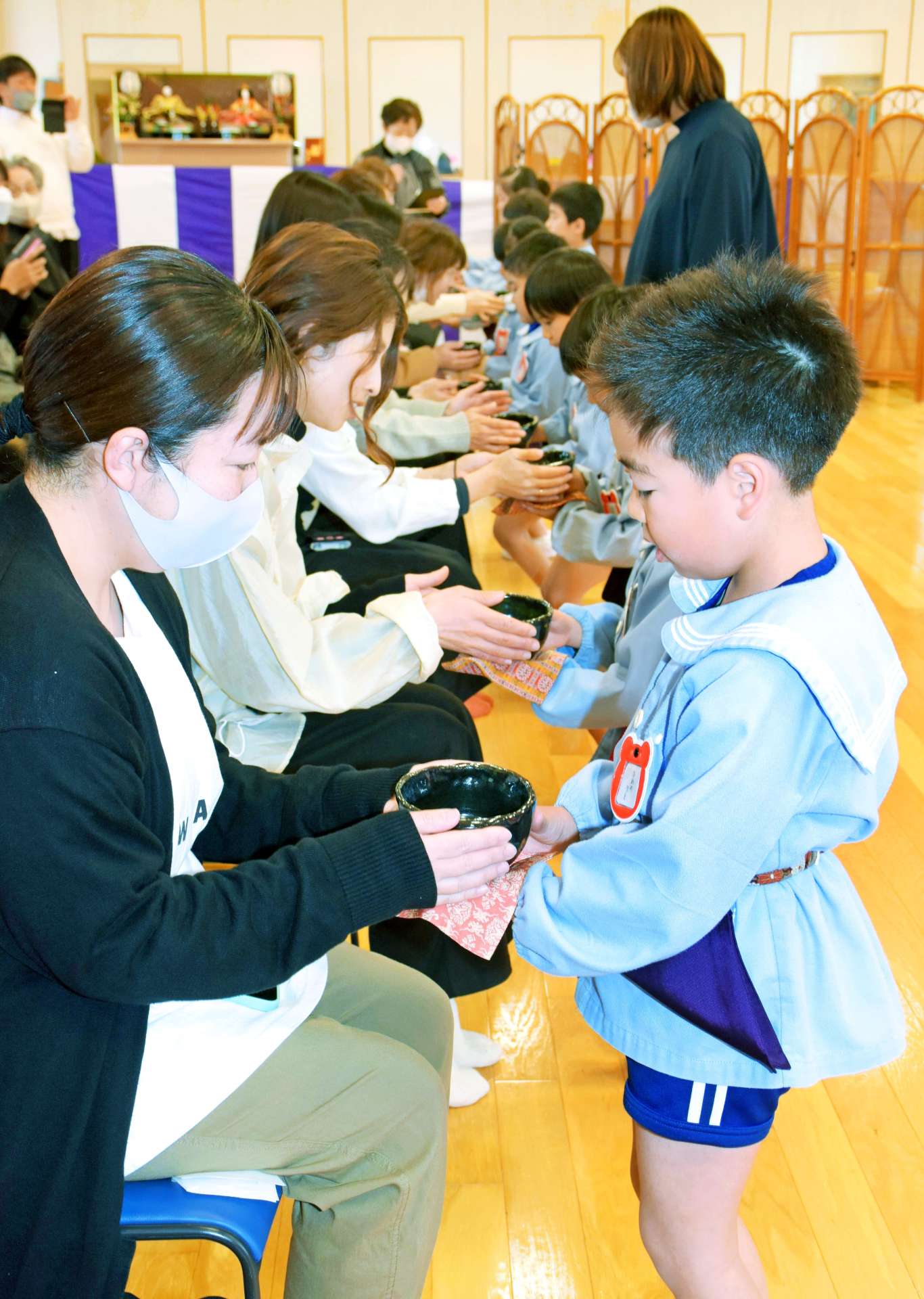 保護者にお茶を運ぶ園児＝８日、指宿市山川のたいせいこども園