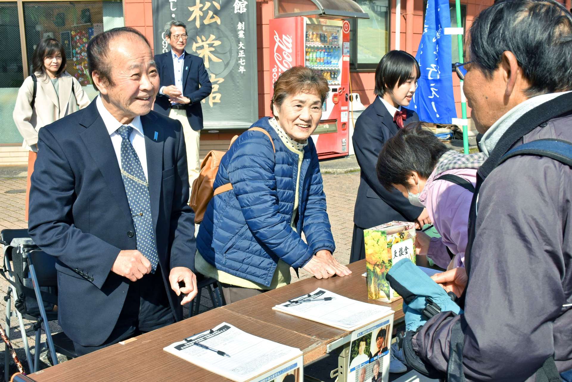 高校生と共に署名活動をする（左から）市川健一さんと龍子さん＝９日、伊佐市大口上町