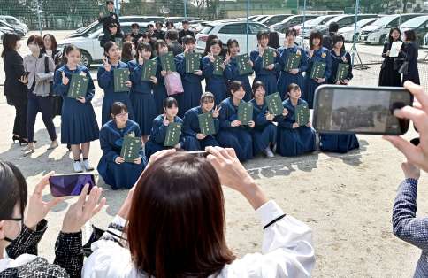 保護者が向けるカメラに笑顔を見せる西紫原中学校の卒業生＝１２日午前、鹿児島市